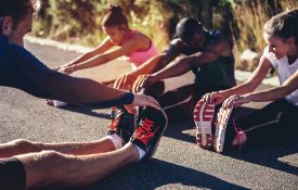 Multi-ethnic group of young adult athletes doing hamstring stretch exercises after a running workout