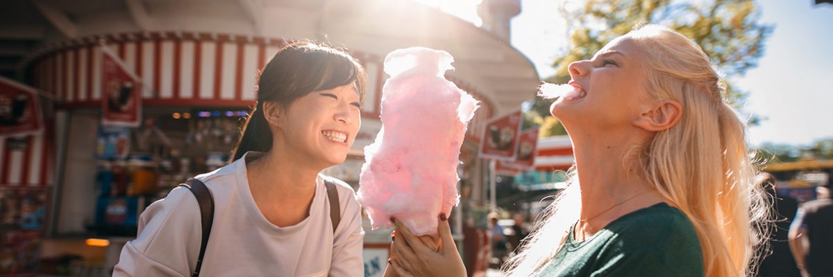 Photo of two young women sharing cotton candy at an amusement park