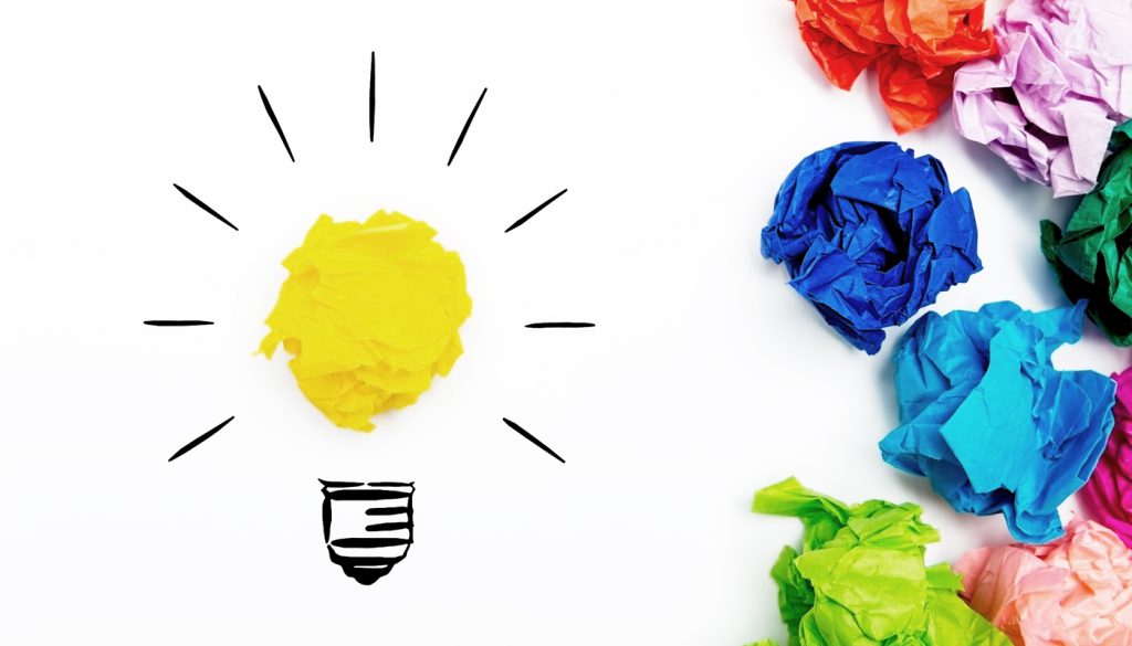 Crumpled paper light bulb over white background, surrounded by crumpled colorful paper.