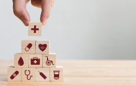 Hand placing wood blocks in a pyramid, each with a symbol representing health care and medicine