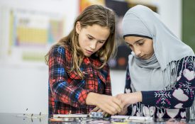 Two girls working together with wires and circuits during science class.