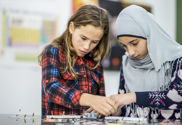 Two girls working together with wires and circuits during science class.