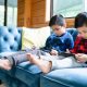 Two young boys sitting on a couch looking at tablets.