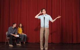 Performer in front of a microphone, doing poorly on his set while two people on stage watch from the side.