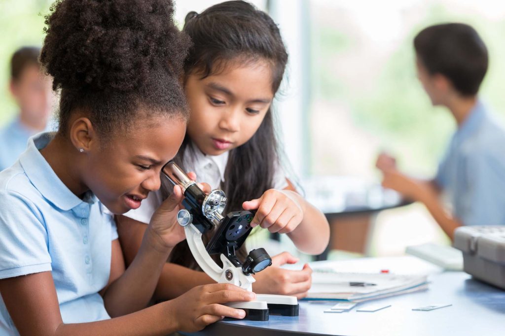 Two young girls looking into a microscope.