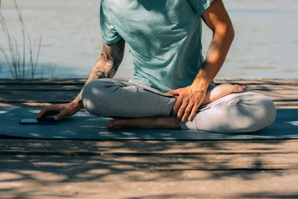 Man sitting on yoga mat and using phone.