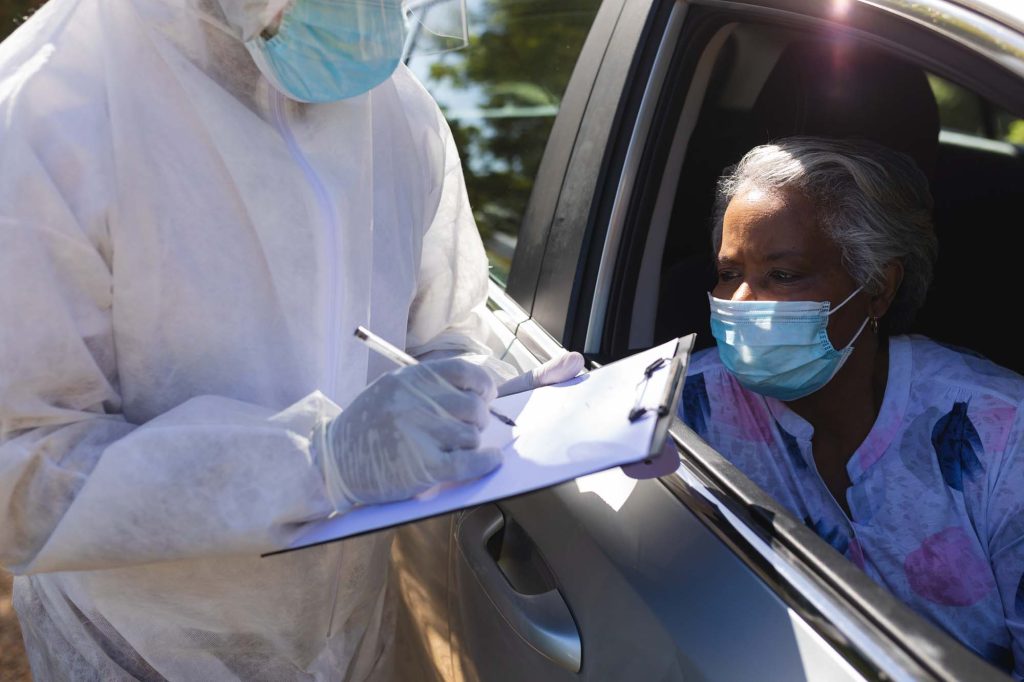 Woman in car giving information to person wearing PPE with clipboard.