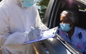 Woman in car giving information to person wearing PPE with clipboard.