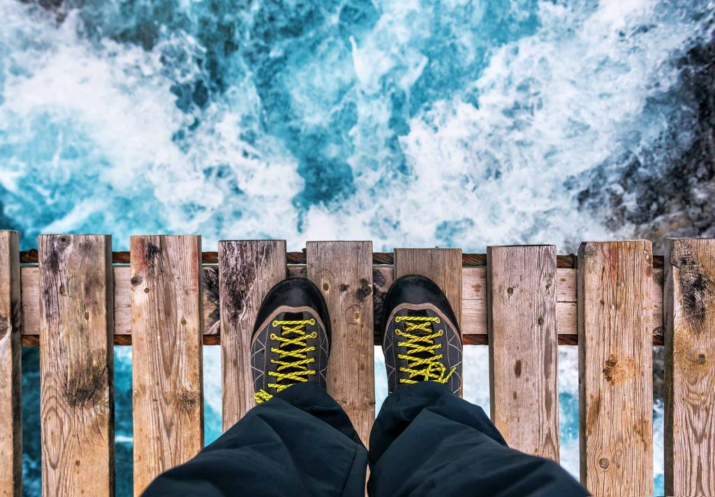 POV of a person looking off of a bridge into white water rapids.