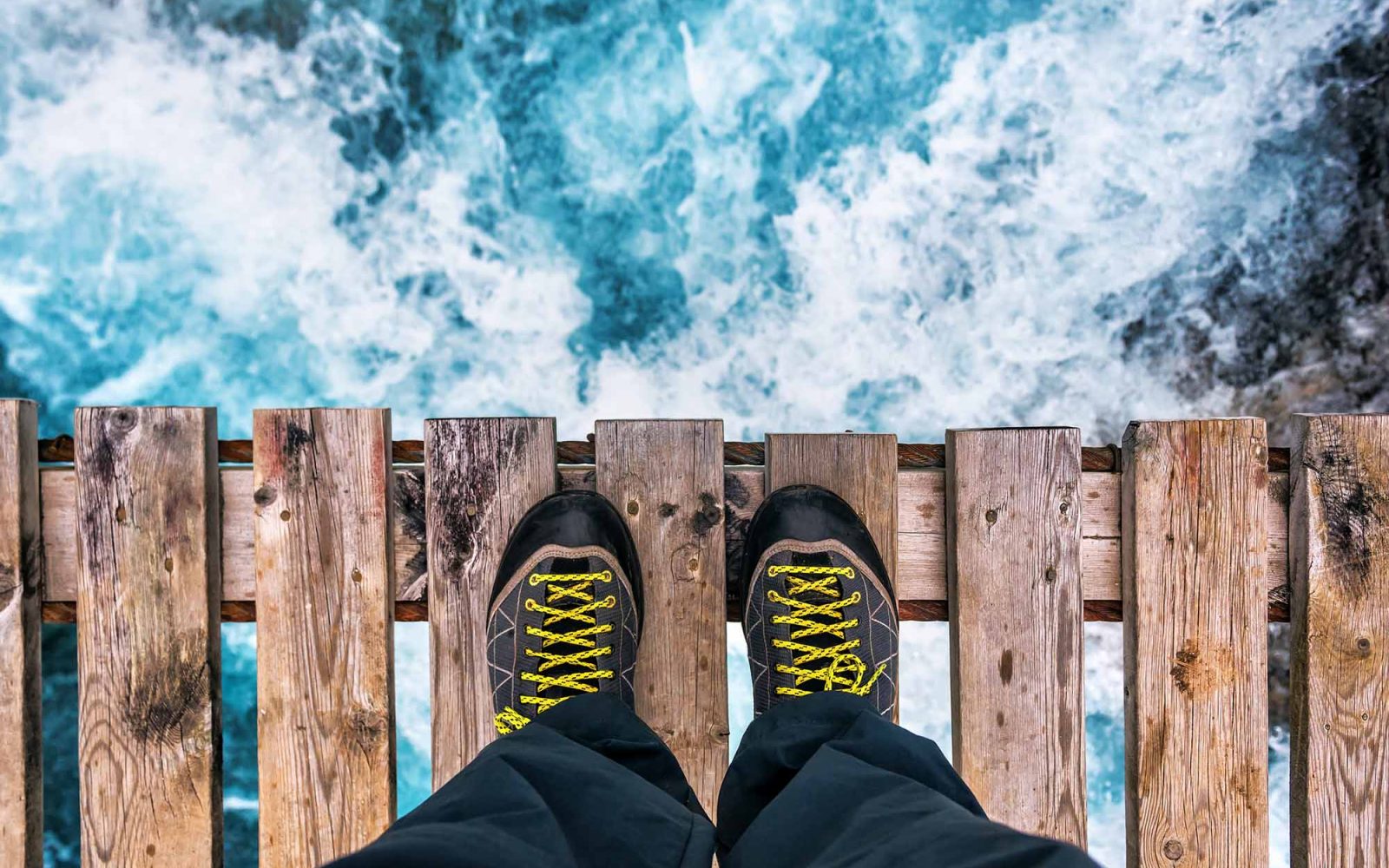 POV of a person looking off of a bridge into white water rapids.