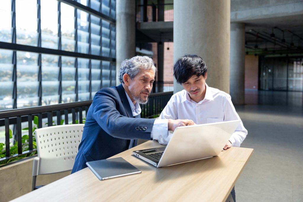 Senior professor giving advice to college student while sitting at a laptop.