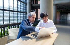 Senior professor giving advice to college student while sitting at a laptop.