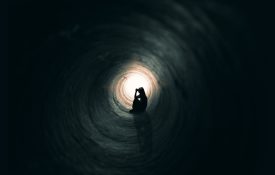 Person sitting in dark tunnel with a light at the end.